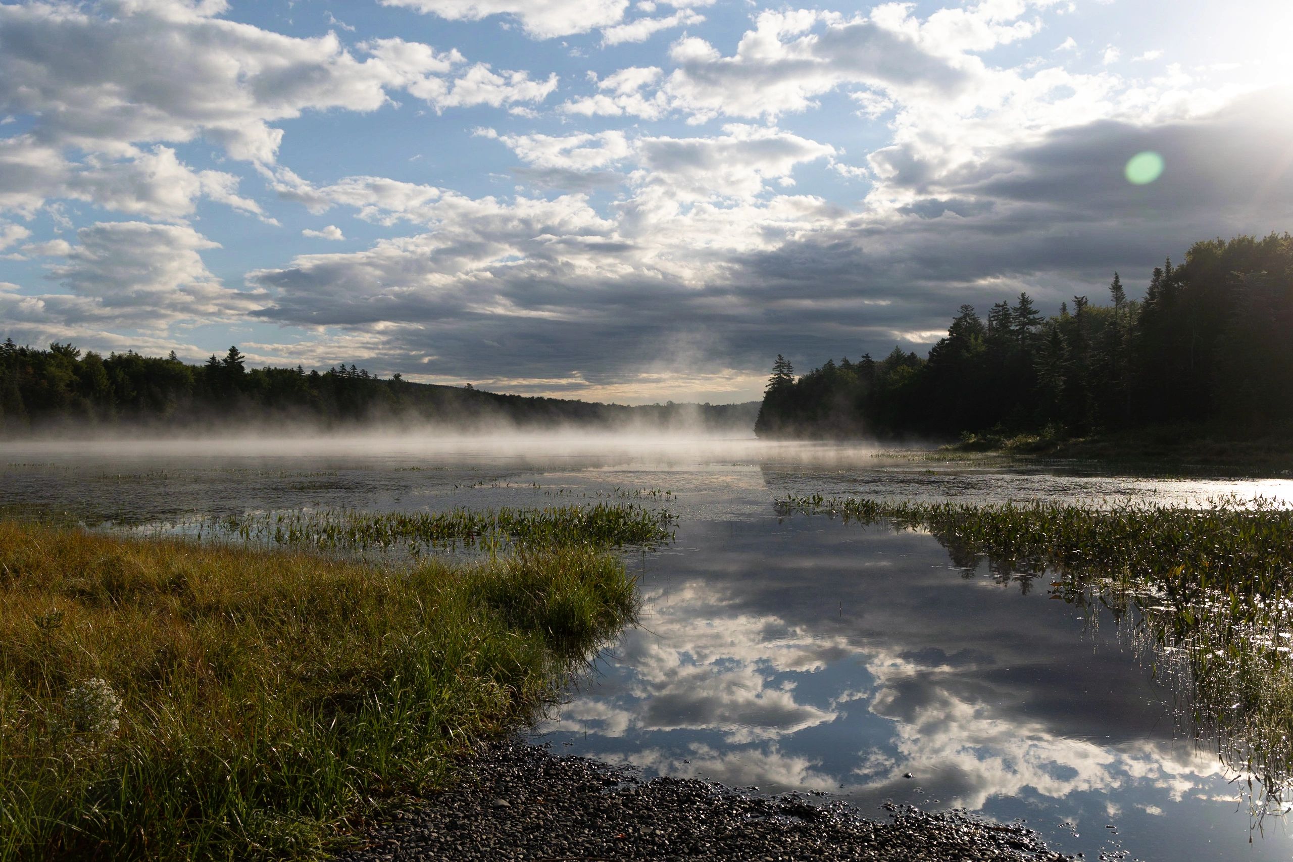 Calm New England lake at sunrise with light fog