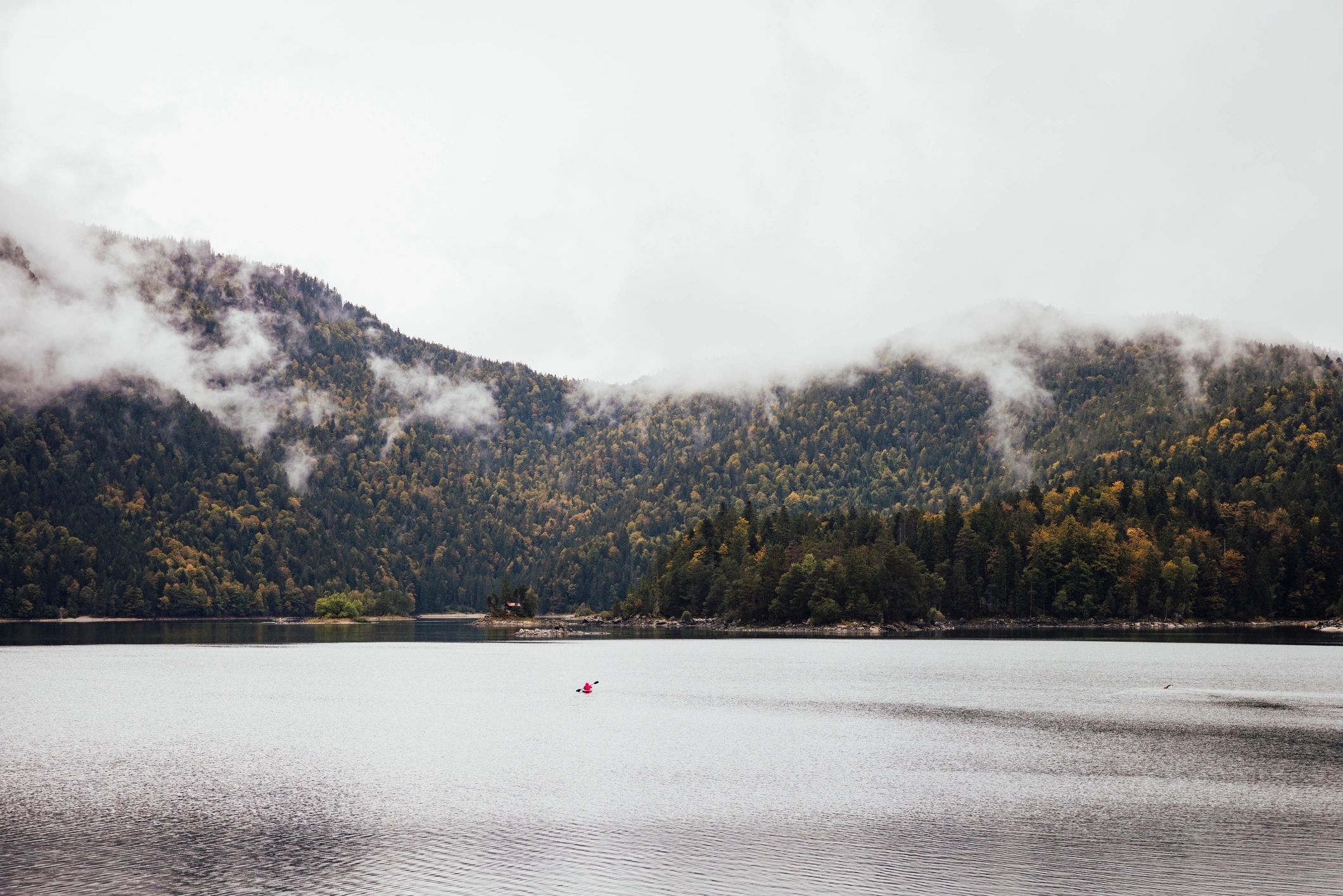 Kayaker on a calm mountain lake with forested shoreline and peaks